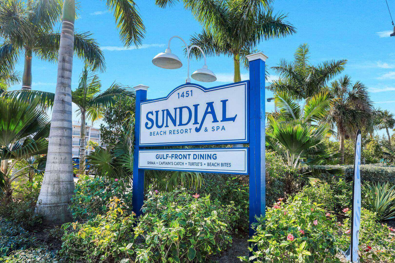 Sundial Beach Resort sign amidst palm trees.